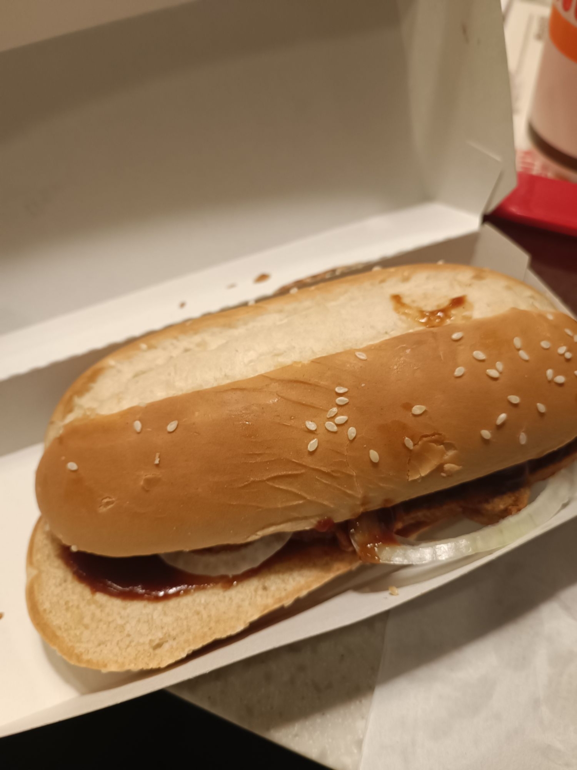 Ein Burger mit Roter Sosse und Zwiebeln in einer Box, appetitlich angerichtet und bereit zum Genießen. 