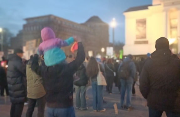 Ein Erwachsener trägt ein Kind auf den Schultern während einer Versammlung bei Dämmerung.