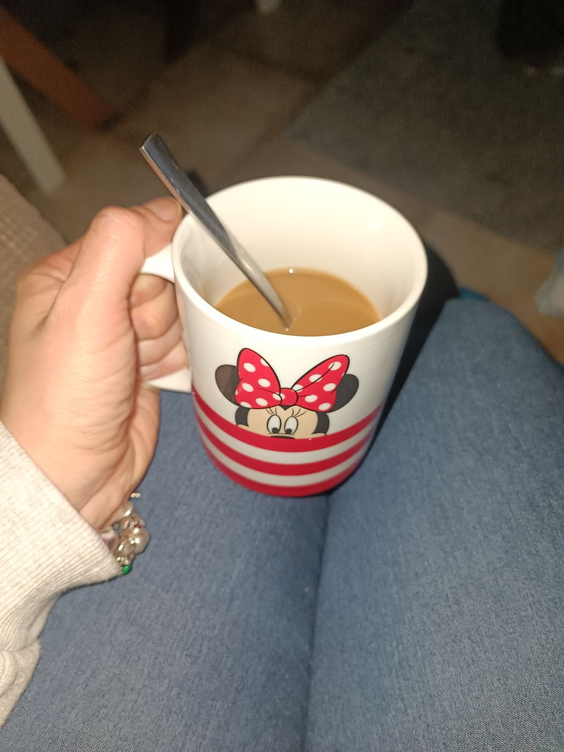 Eine Hand hält eine Tasse mit Minnie Maus Design, gefüllt mit Kaffee und einem Löffel.