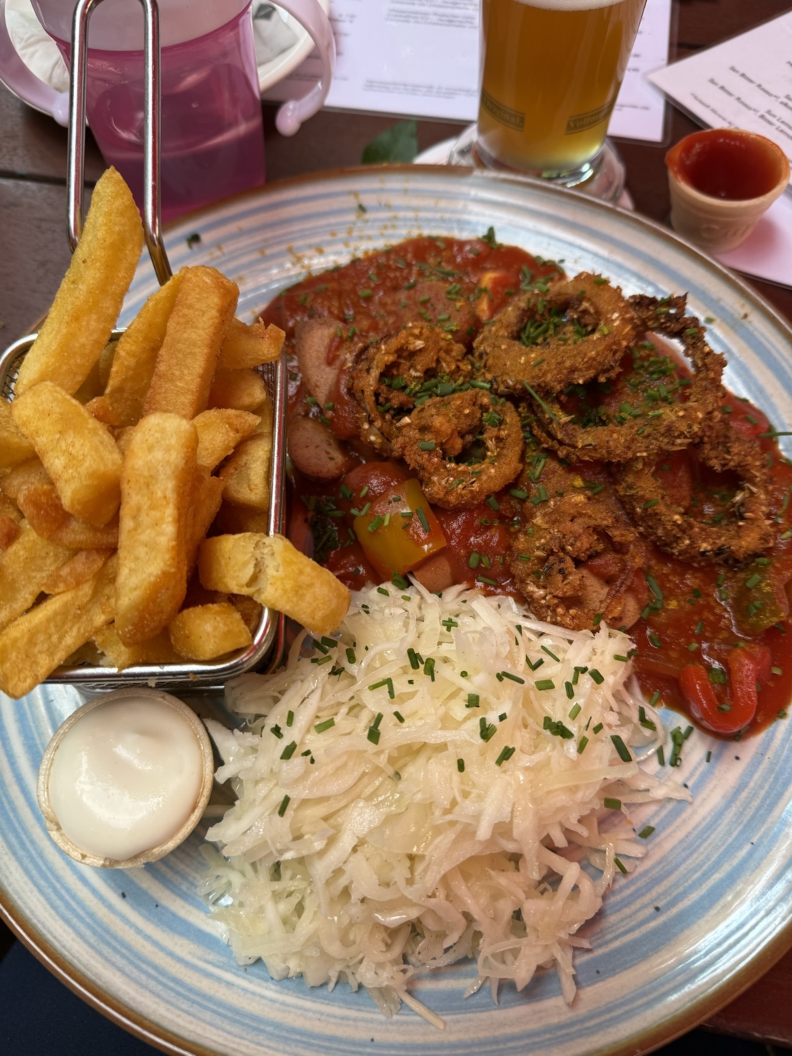 Ein Teller mit frittierten Zwiebelringen, Pommes Frites und Sauerkraut in einer roten Sauce.