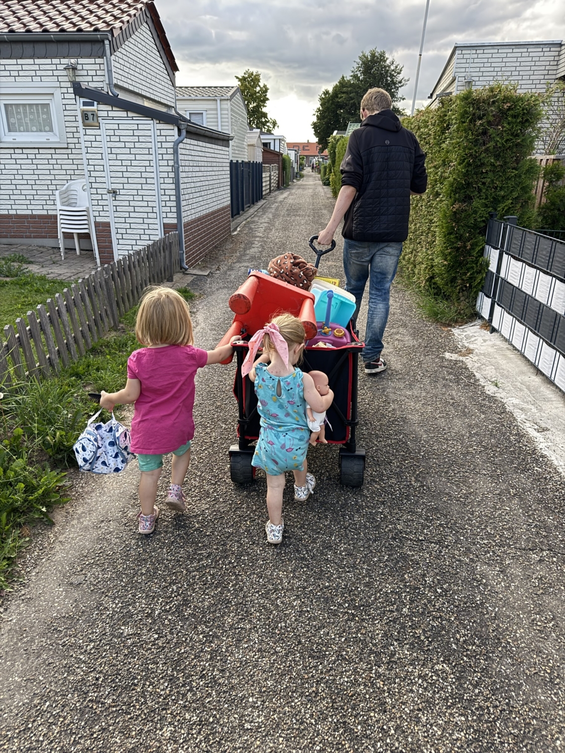 Eine Familie zieht einen Wagen mit verschiedenen Gegenständen auf einem Weg zwischen Mobilheimen.