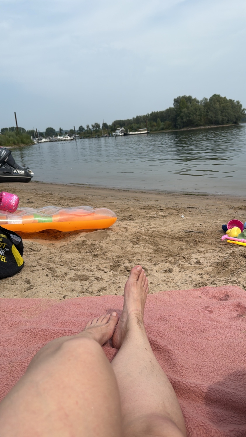 Füße auf einem Handtuch am Strand mit Wasser im Hintergrund. Strand unseres Dauercamperplatzes