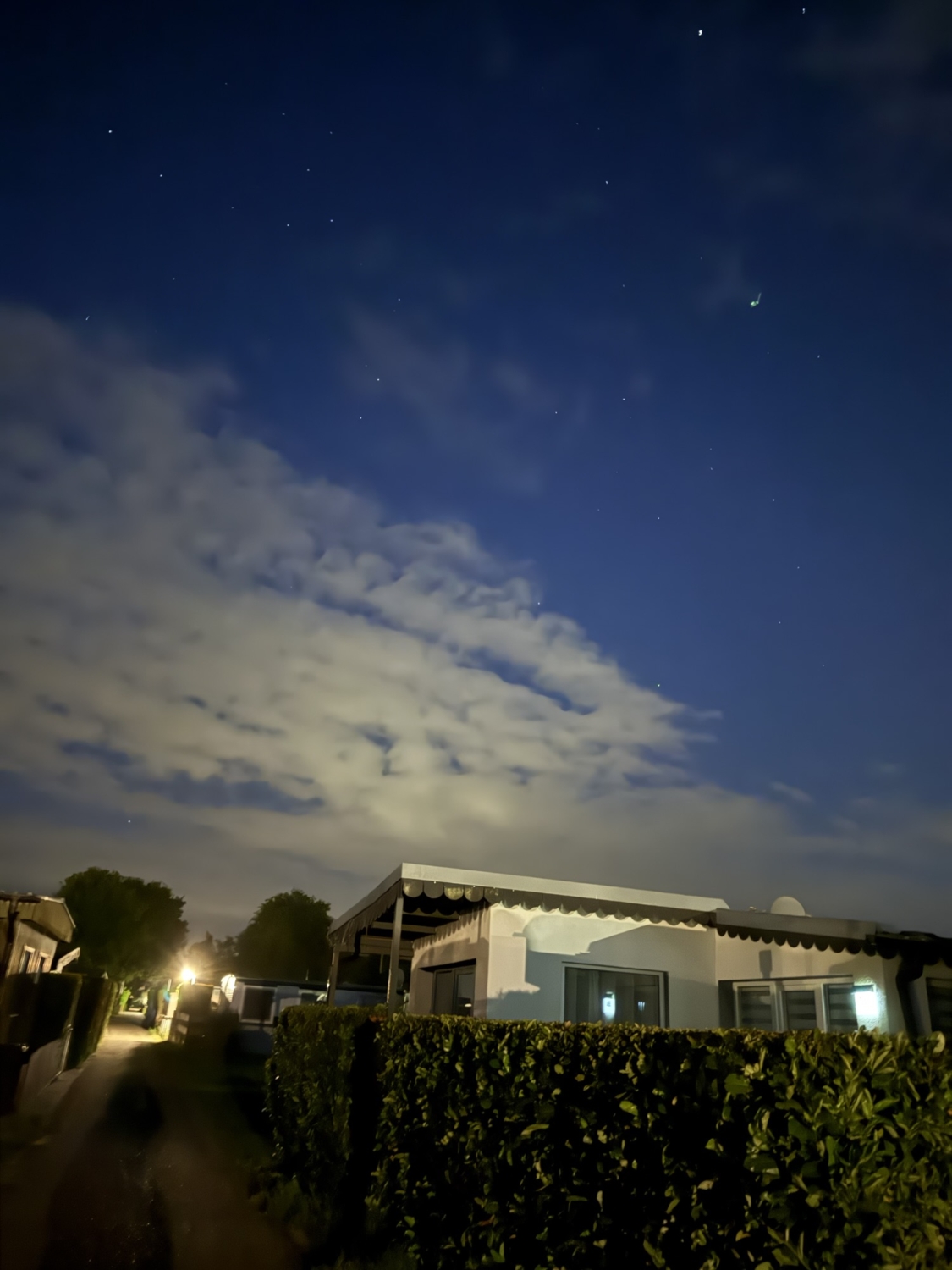 Nachtaufnahme eines Mobilheims unter einem klaren Sternenhimmel mit Wolken.