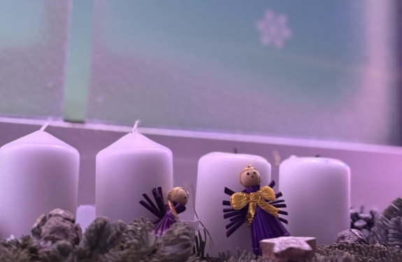 Zwei handgefertigte Engel aus Holz mit lila und gelben Details neben weißen Kerzen auf einem Adventskranz.