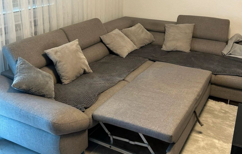 Grau gepolsterte Eckcouch mit mehreren Kissen und einer ausziehbaren Matratze.