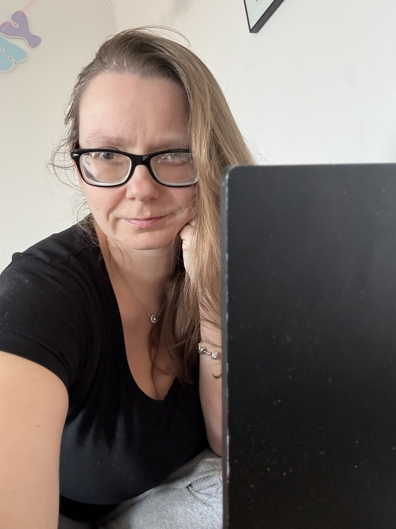 Frau mit langen Haaren und Brille, die an einem Laptop sitzt und in die Kamera schaut.