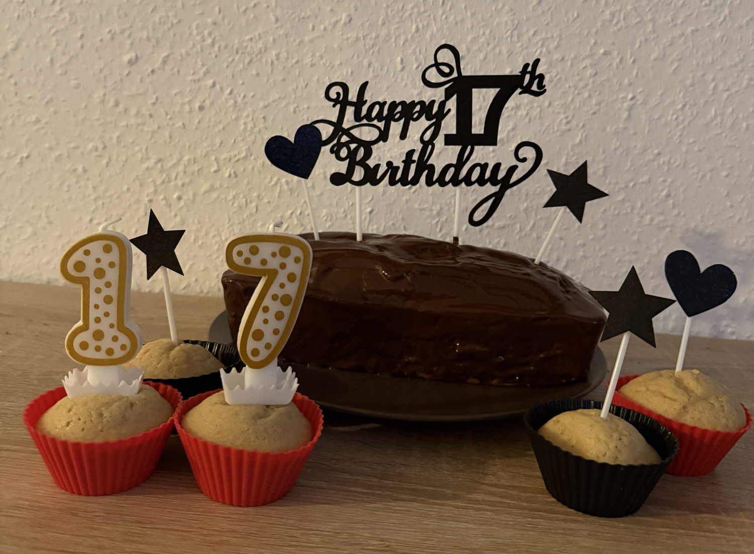 Ein Schokoladenkuchen mit Muffins, Kerzen mit der Zahl 17 sowie schwarzen Sternen und Herzen auf einem Geburtstagstisch.